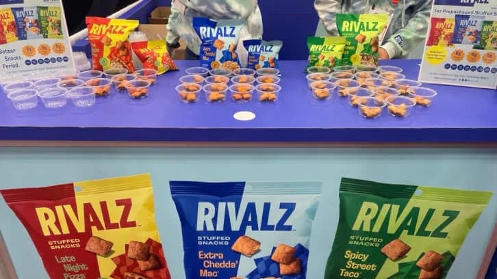 매장 선반에 라이벌즈(Rivalz) 간식 포장들이 진열돼 있고 앞쪽에 시식용 샘플 용기가 놓여 있다