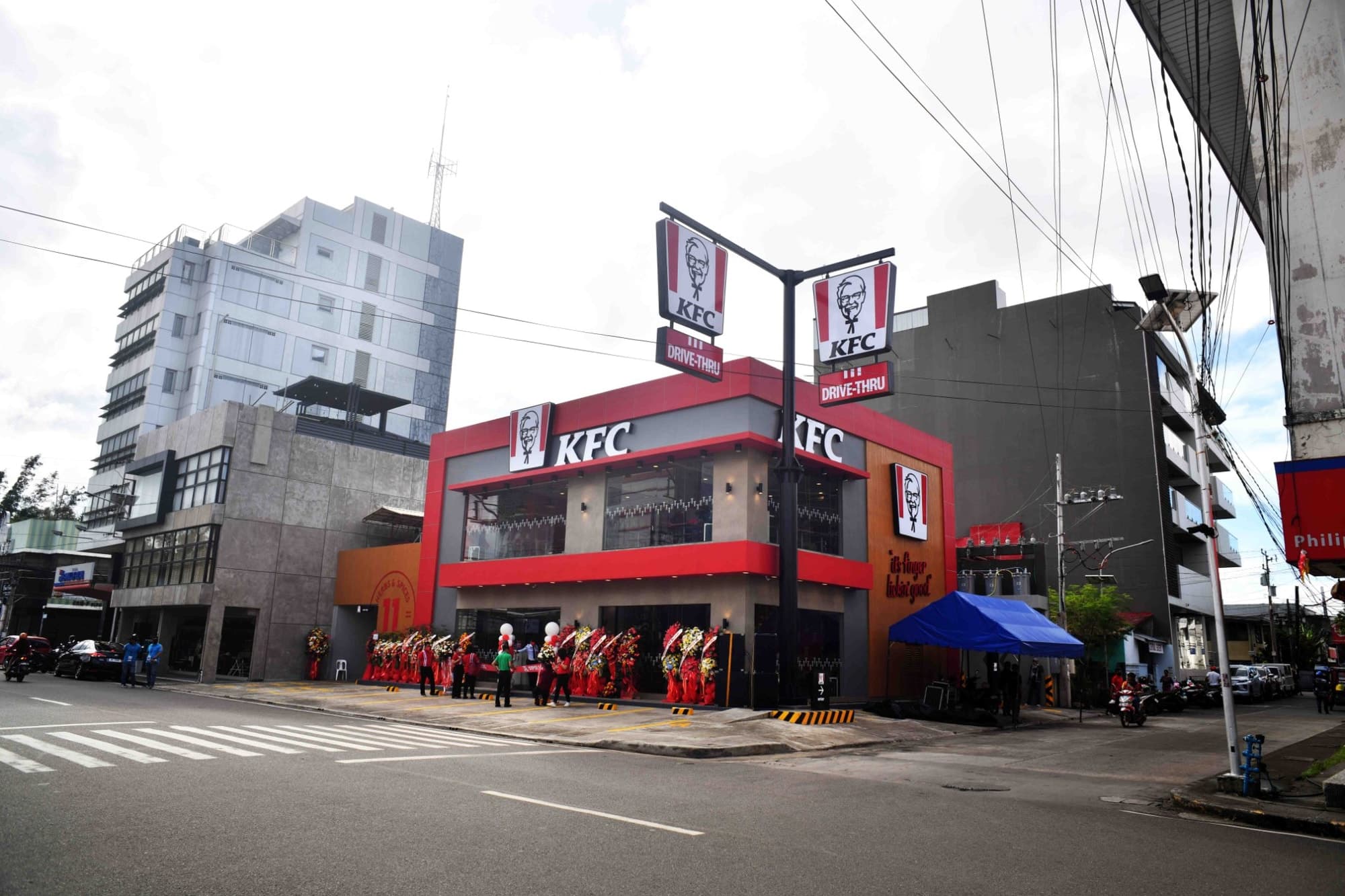 KFC 매장이 도로 옆에 위치해 있으며 간판에 KFC 로고와 드라이브-스루 표지판이 보인다